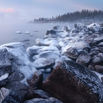 Rocky shoreline covered in frost before sunrise, with mist and soft pink clouds